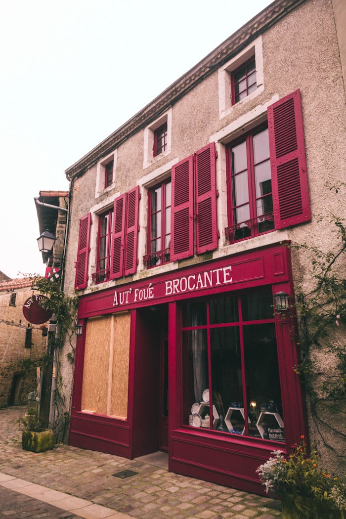 Rustic building in Parthenay, France with red shutters and vintage signage.