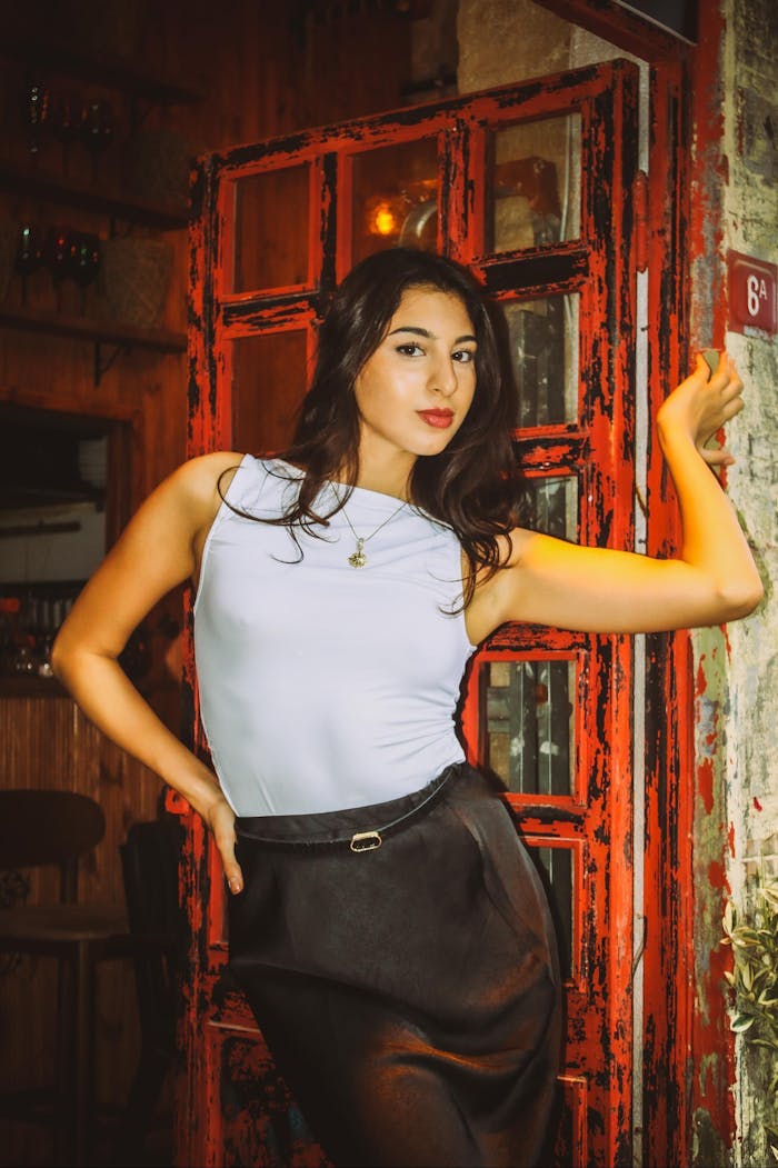 Elegant woman poses confidently near vintage red door, wearing chic fashion.